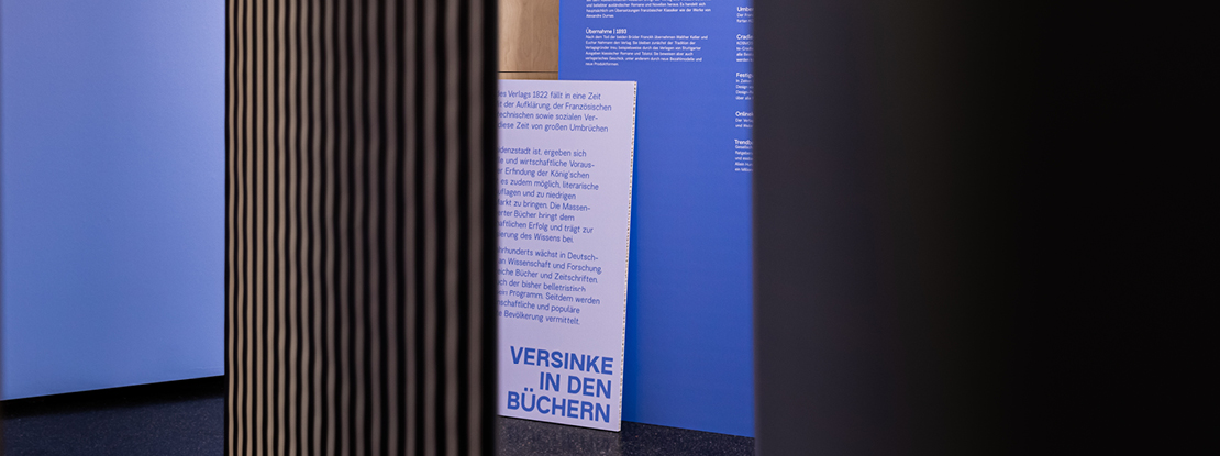 VISUELL Szenografie: 200 Jahre KOSMOS, Jubiläumsausstellung VISUELL Szenografie: Ausstellungsrundgang: zwei blaue Texttafeln – Aufschrift: Versinke in den Büchern