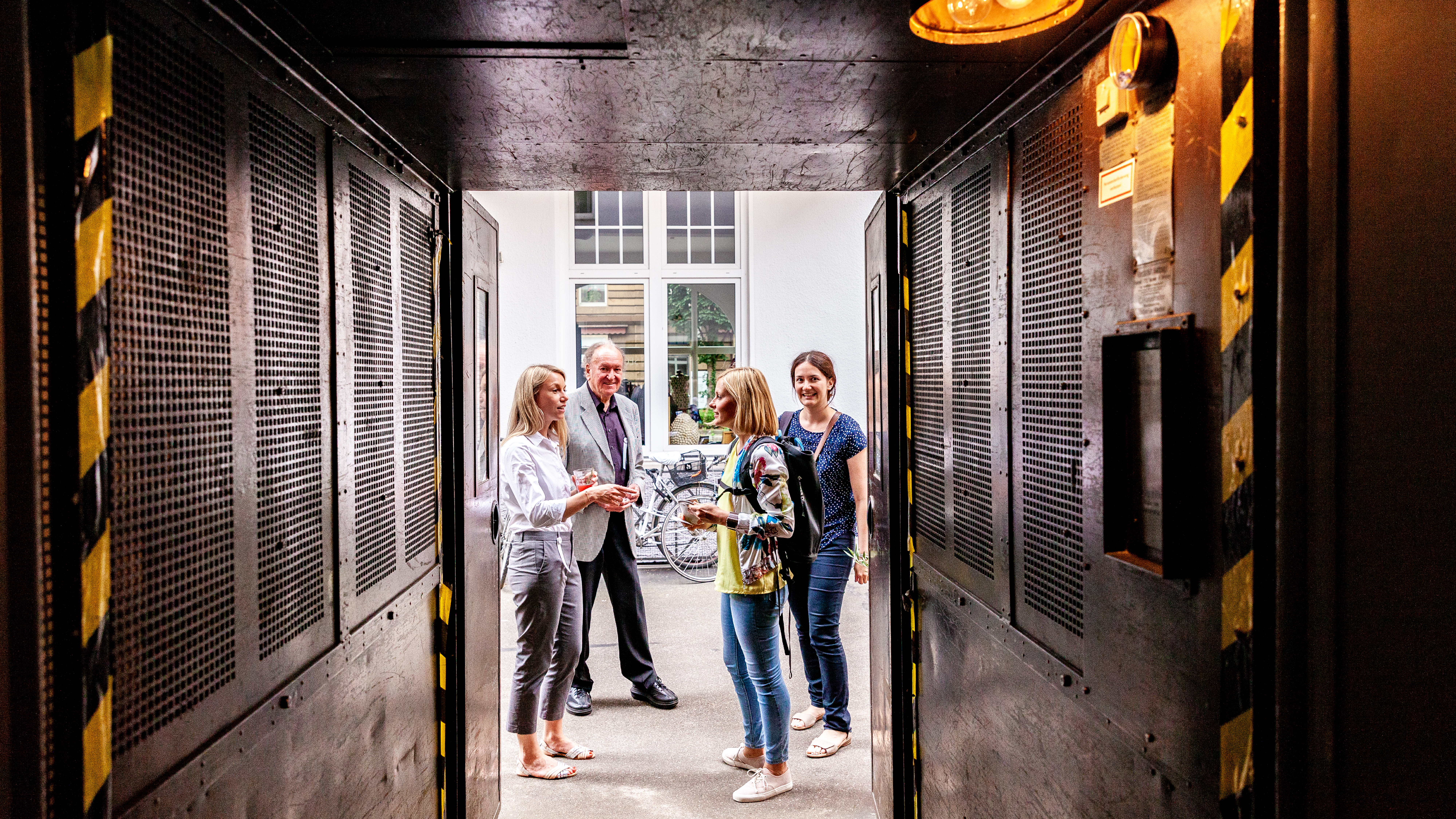 VISUELL Blogbeitrag: Event unterm Dach– das Olivenöl-tasting: Vier Personen stehen im Vorhof von VISUELL und unterhalten sich