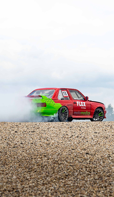 VISUELL Blogbeitrag: Titelstory des DeinsMeinsUnsers: Ein driftendes rot/grünes Auto zieht eine Staubwolke hinter sich her