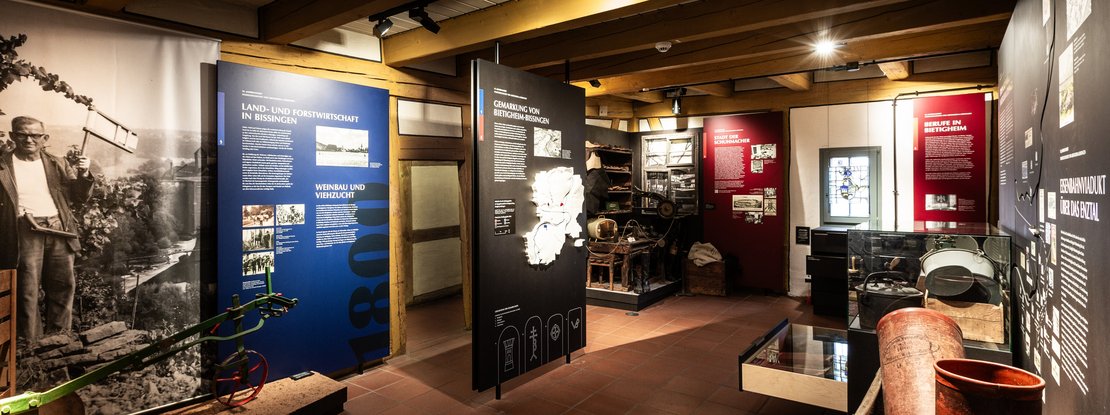 VISUELL Scenography: Permanent exhibition at Hornmoldhaus: Exhibition space with freestanding, colour-coded themed steles on agriculture and forestry, local landmarks and professions in Bietigheim-Bissingen. Historical exhibits such as tools and equipment are integrated into the chronological presentation in display cases and open displays.
