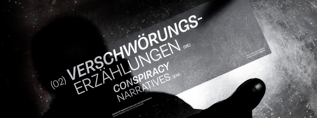 VISUELL Szenografie: Sonderausstellung: Anti Anti 2.0: Titelgrafik „Verschwörungserzählungen / Conspiracy Narratives“ auf schwarzem Hintergrund; diagonale Typografie als visuelle Intervention, die bestehende Narrative hinterfragt.