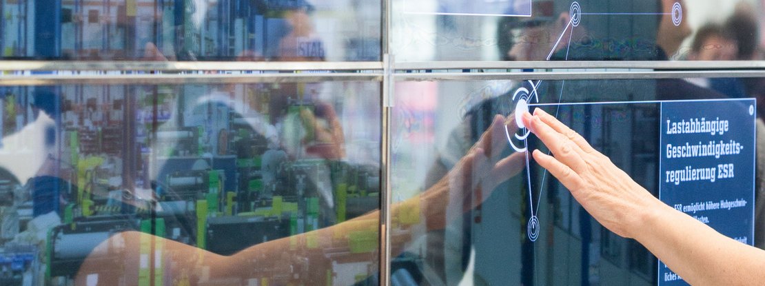 VISUELL Szenografie: Messestand STAHL CraneSystems: Nahaufnahme einer Hand, die den interaktiven Touchscreen der Medieninstallation bedient