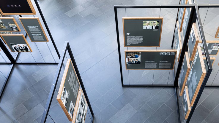 VISUELL Szenografie: Jubiläumsausstellung: Blick von oben auf das Ausstellungssystem mit Metallkonstruktion, Stahlseilen und darin befestigten Holzrahmen mit Informationstafeln in verschiedenen Formaten mit unterschiedlichem Inhalt.