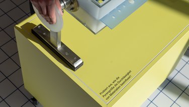 VISUELL Szenografie: Wissenschaftsausstellung: Detailaufnahme eines interaktiven Exponats zu Selektionsmechanismen in der Ausstellung „Was kann Katalyse?“. Eine Hand bedient das drehbare Exponat, welches darstellt wie die Porengröße die Durchlässigkeit von Materialien beeinflusst.