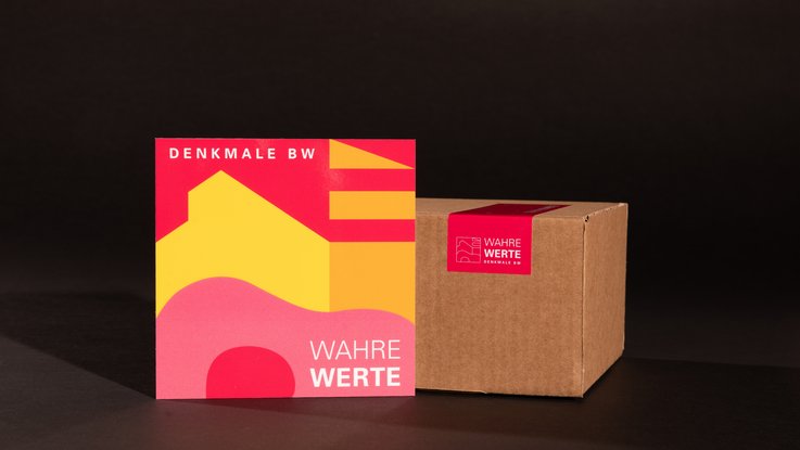 VISUELL Kommunikationsdesign: Ansicht der Denkmalplakette des Landesamts für Denkmalpflege, welche am dazugehörigen Karton mit abgestimmtem Verpackungssiegel lehnt