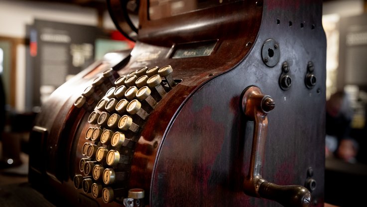 VISUELL Scenography: Permanent exhibition at Hornmoldhaus: Detail of a historical cash register with numbered metal keys and a side-mounted hand crank, displayed as part of the exhibition on the history of trade.