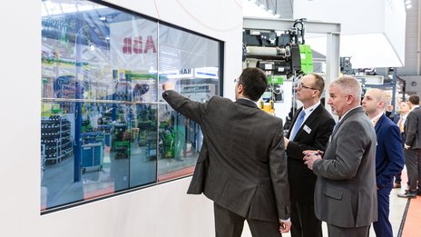 VISUELL Szenografie: Messestand STAHL CraneSystems: Vier Besucher bedienen die interaktive Medieninstallation über einen Touchscreen  