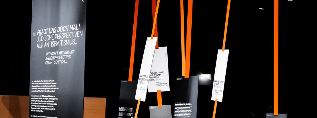 VISUELL Szenografie: Sonderausstellung: Anti Anti 2.0: Mehrere Interventionselemente mit schwarzen Tafeln und weißen Texten; Bänder erzeugen eine räumliche Struktur und lenken die Wahrnehmung neu.