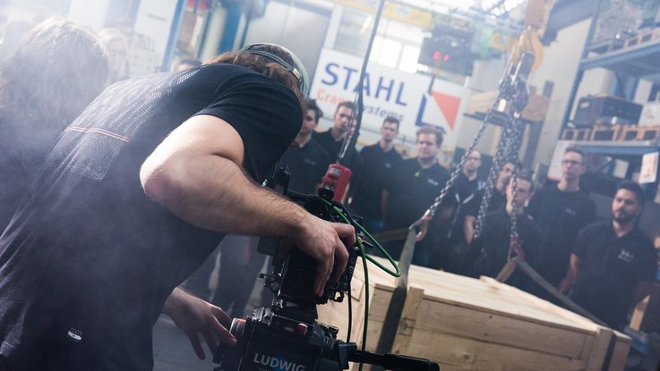 VISUELL Kommunikationsdesign: Kino-Werbespot für STAHL CraneSystems: Der Kameramann in Action mit einer großen Gruppe an Menschen im Werk von STAHL CraneSystems mit dramatischem Nebel