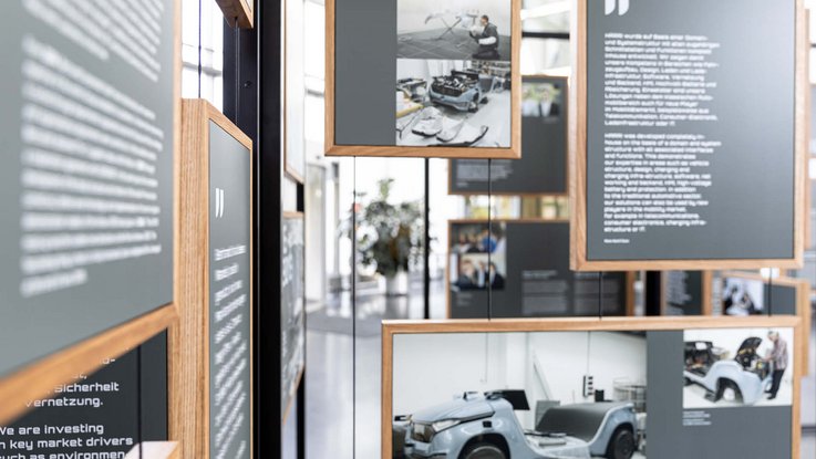 VISUELL Szenografie: Jubiläumsausstellung: Detail einiger Informationstafeln mit weißer Typografie auf anthrazitfarbenem Grund in einem Holzrahmen, im Hintergrund sind weitere Informationstafeln zu sehen.