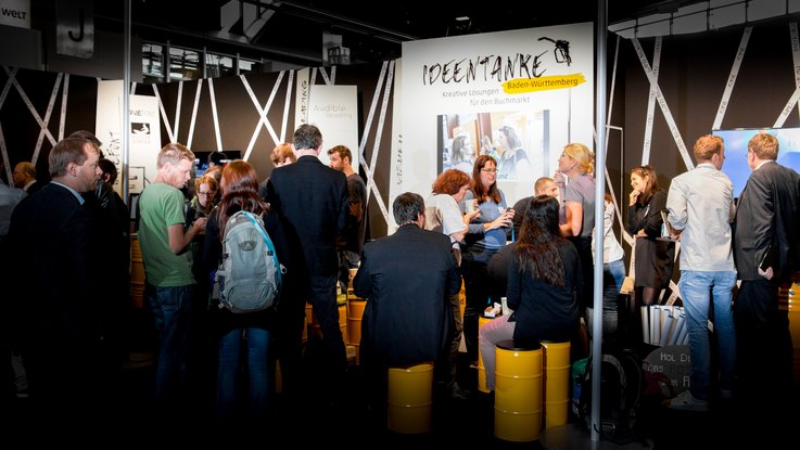 VISUELL Szenografie: Messestand Ideentanke MFG: Gesamteindruck des Messestands mit zahlreichen Besuchenden 