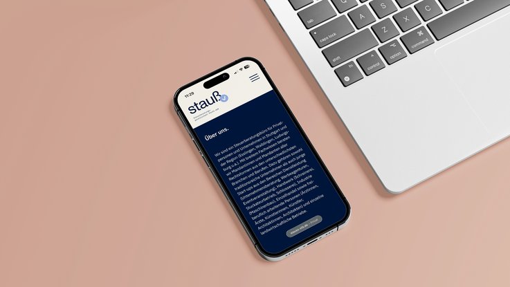 VISUELL Kommunikationsdesign: Corporate Design Stauß: Mobile Website auf einem Smartphone neben einem Laptop; die Ansicht zeigt das responsive Webdesign mit Logo, Navigation und einer klar gegliederten Inhaltsseite auf roséfarbenem Hintergrund.