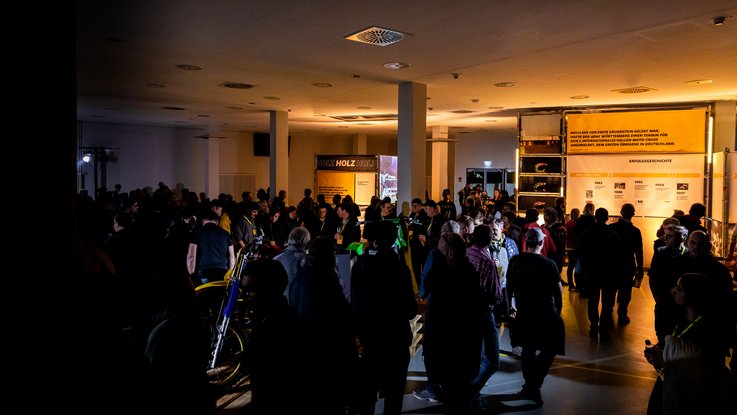 VISUELL Szenografie: Ausstellung: Zahlreiche Besucherinnen und Besucher bewegen sich durch die Ausstellung; die beleuchteten Bannertafeln setzen thematische Highlights.