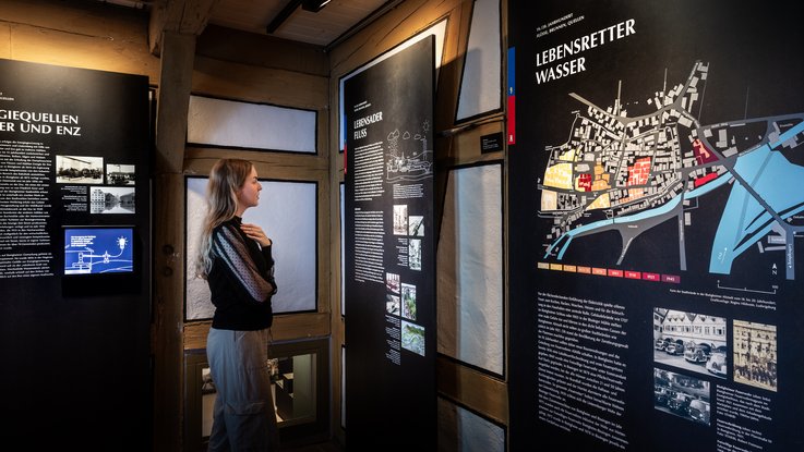 VISUELL Scenography: Permanent exhibition at Hornmoldhaus: Visitor in front of large-format, graphically designed information boards on energy sources, river landscapes and urban development. The themes of the river as a lifeline and water as a lifesaver are vividly conveyed in the historic half-timbered room.