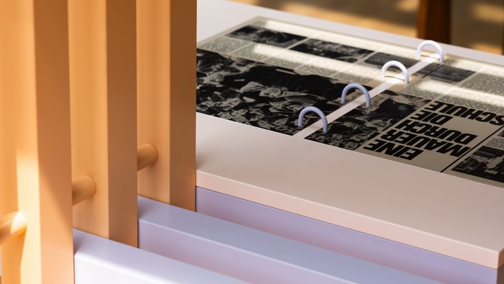 VISUELL Szenografie: Wanderausstellung „Jubiläum. 75 Jahre Verfassung NRW“ für die Stiftung Haus der Geschichte Nordrhein-Westfalen VISUELL Szenografie: Wanderausstellung: Detailaufnahme eines Ausstellungstisches mit aufgeklappten Zeitungsseiten aus den 1960er-Jahren, Überschrift „Eine Mauer durch die Schule“.