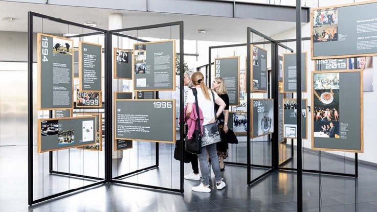 VISUELL Szenografie: Jubiläumsausstellung: Drei Besucherinnen stehen inmitten der Ausstellung und betrachten die Inhalte.