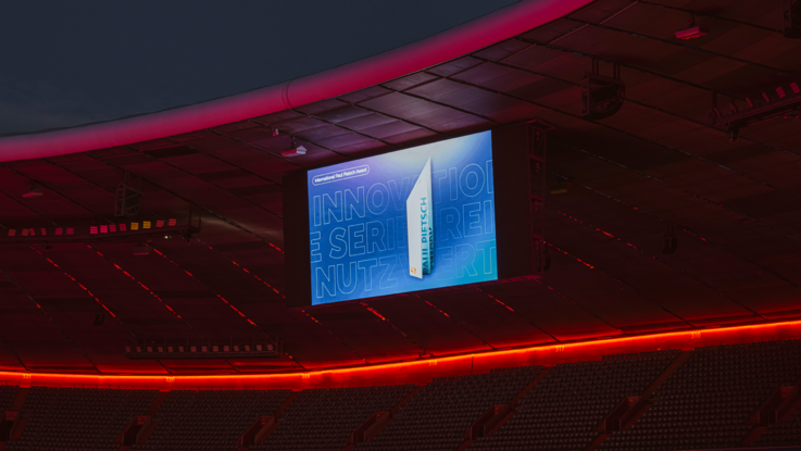 VISUELL Szenografie: Event „NEXT LEVEL“: Übertragung der Präsentation der Veranstaltung auf die große Stadion-LED der Allianz Arena, mittlerweile ist es dunkel und die Allianz Arena leuchtet rot.