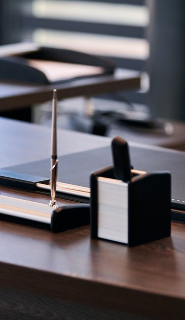 VISUELL Kommunikationsdesign: Corporate Design Stauß: Nahaufnahme von Schreibgerät, Kartenhalter und Schreibtischaccessoires in dunklen Materialien; die Bildsprache vermittelt Präzision, Ordnung und Professionalität im Arbeitsumfeld der Steuerberatung.