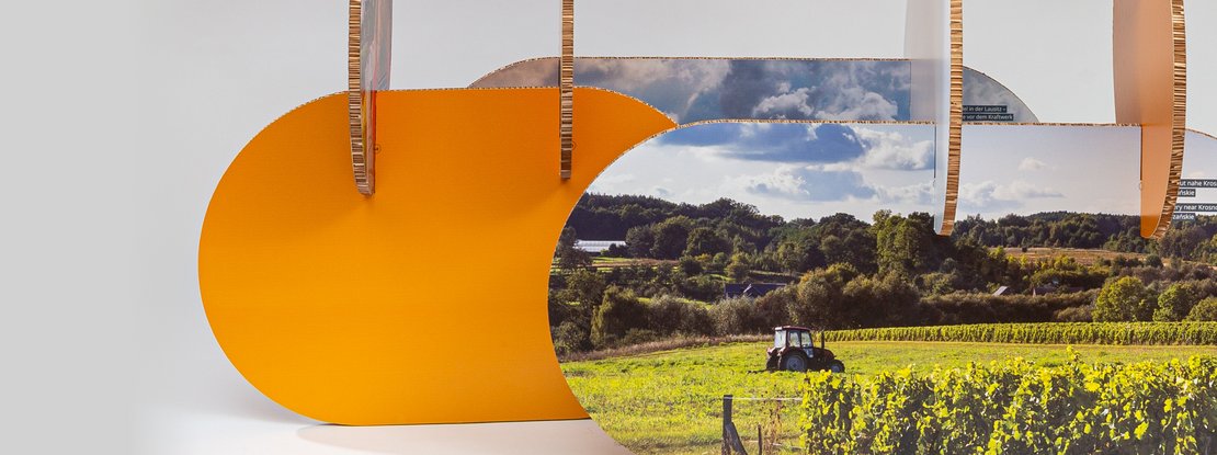 VISUELL Szenografie: Wanderausstellung „Common Grounds – Über Grenzen mitgestalten“ für die Robert Bosch Stiftung GmbH VISUELL Szenografie: Wanderausstellung Robert Bosch Stiftung GmbH: Panoramatische Teilansicht eines modularen Ausstellungselements mit organisch geschwungenen, orangefarbenen Formen und integrierten Landschaftsfotografien; senkrechte und waagerechte Elemente prägen die Komposition.