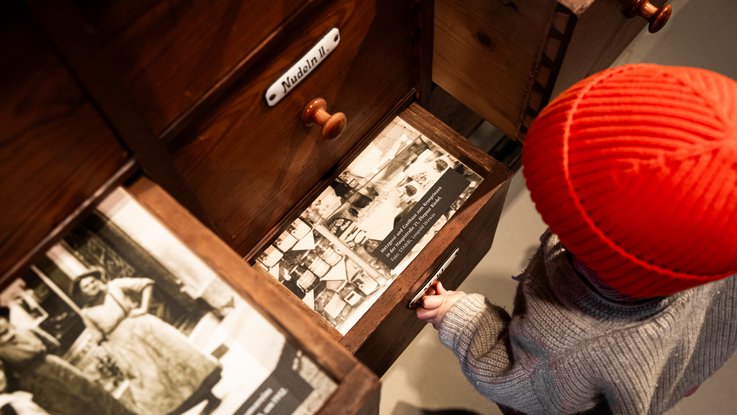 VISUELL Scenography: Permanent exhibition at Hornmoldhaus: A child wearing a red cap opens a historic drawer in the merchant's cabinet and discovers photographs and information about the city's history. Interactive elements make the exhibition a playful experience.