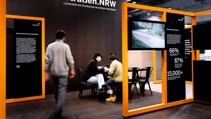 VISUELL Scenography: Straßen.NRW stand at InfraTech 2026: Visitors move freely through the open-plan stand; sightlines between the orange modules allow for intuitive orientation and draw the eye to the information on display.