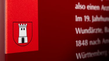 VISUELL Scenography: Permanent exhibition at Hornmoldhaus: Detail of a red exhibition panel with city coat of arms and white typography. The colour coding aids orientation within the chronological presentation.