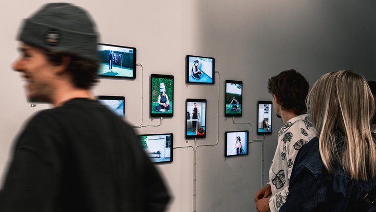 VISUELL Blogbeitrag: ADC Talent Festival 2025 „Goldenes Konfetti – Silberner Nagel“ VISUELL Blogbeitrag: ADC Talent Award 2025: Besucher:innen stehen vor den Tablets der Videoinstallation „353 – Die (zu)Vielzahl meiner Dinge“ und betrachten die ausgestellten Videoszenen.
