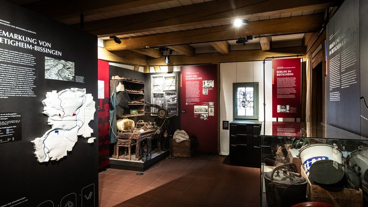 VISUELL Scenography: Permanent exhibition at Hornmoldhaus: Exhibition area with large-format black thematic stele on the district of Bietigheim-Bissingen and colour-coded red information boards. Historical workshop staging and exhibits in display cases are integrated into the chronological presentation.