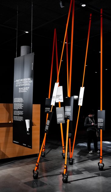 VISUELL Szenografie: Sonderausstellung: Anti Anti 2.0: Mehrere Interventionselemente mit schwarzen Tafeln und weißen Texten; Bänder erzeugen eine räumliche Struktur und lenken die Wahrnehmung neu.