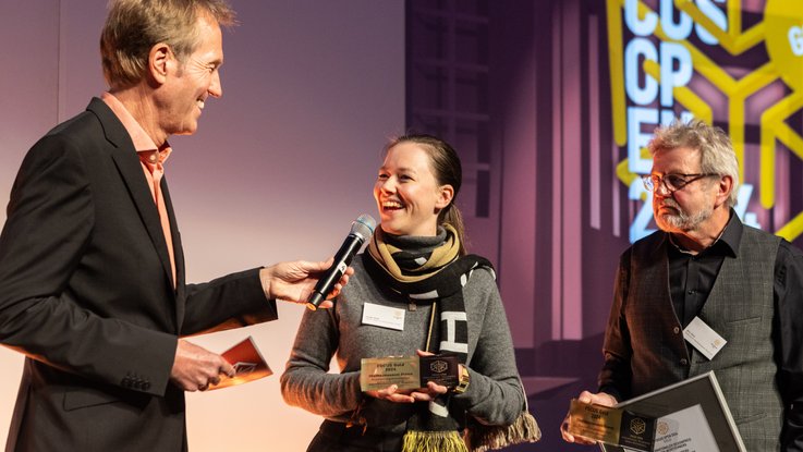 VISUELL Blogbeitrag: VISUELL gewinnt den FOCUS OPEN 2024 Gold für das Obstbaumuseum Glems VISUELL Blogbeitrag: FOCUS OPEN Award 2024 Gold: Geschäftsführering Laureen Seider wird auf der Bühne interviewt, daneben steht Willy Müller aus dem Förderverein Obstbaumuseum Glems mit der gerahmten Urkunde