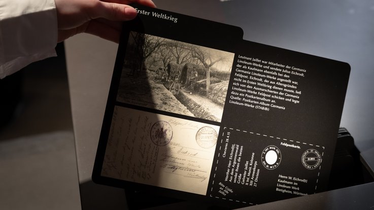 VISUELL Scenography: Permanent exhibition at Hornmoldhaus: Detail of an interactive map on the theme of the First World War, with historical photographs, field postcards and explanatory text. A hand holds the element above a black exhibition table.