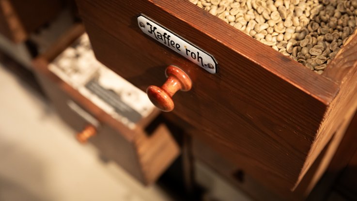 VISUELL Scenography: Permanent exhibition at Hornmoldhaus: Close-up of a historical drawer labelled 'Kaffee roh' (raw coffee), filled with green coffee beans. The exhibit refers to trade in goods and colonial goods in the merchant's shop.