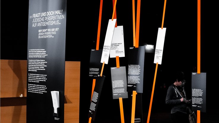 VISUELL Scenography: Special exhibition: Anti Anti 2.0: A series of installation elements featuring black panels and white text; ribbons create a spatial structure and redirect the viewer’s perception.
