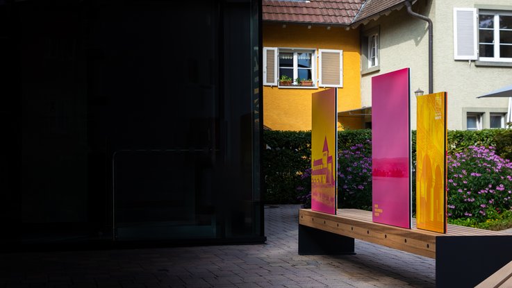 VISUELL Szenografie: Wahre Wunderbänke: Gesamteindruck der Rückseite einer Sitzbank mit Informationstafeln mit großen, aufmerksamkeitsstarken Fotos