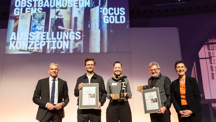VISUELL Blogbeitrag: VISUELL gewinnt den FOCUS OPEN 2024 Gold für das Obstbaumuseum Glems VISUELL Blogbeitrag: FOCUS OPEN Award 2024 Gold: Fünf Personen posieren auf dem Bühne mit der gerahmten Urkunde und der Trophäe des FOCUS OPEN Award 2024 Gold