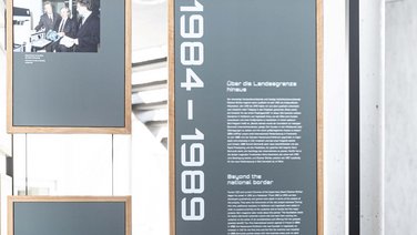 VISUELL Szenografie: Jubiläumsausstellung: Unterschiedliche Informationstafeln, davon eine mit plakativen Jahreszahlen am linken Rand sowie Fließtext mit Überschriften.
