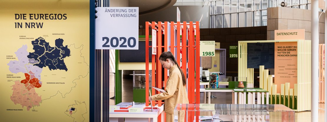 VISUELL Szenografie: Wanderausstellung: Blick in die Ausstellung mit farbigen Modulen und Informationstafeln zu Themen wie Europa, Datenschutz und Verfassungsänderungen. Eine Person betrachtet Exponate zwischen farbigen Rahmen.