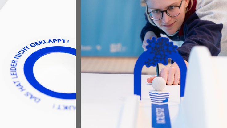 VISUELL Szenografie: Wissenschaftsausstellung: Links: Detailaufnahme einer blauen Beklebung des Exponats „Minigolf und Katalyse“. Rechts: Frontale Nahaufnahme einer Besucherin die dieses Exponat mit einem Schäger bedient und durch einen blauen Bogen zielt.