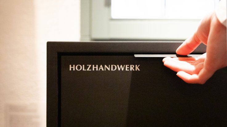 VISUELL Scenography: Permanent exhibition at Hornmoldhaus: Detail of an interactive drawer labelled 'Woodworking'. A hand opens the element, inviting visitors to discover contents relating to historical crafts.