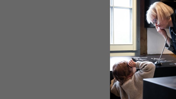 VISUELL Scenography: Permanent exhibition at Hornmoldhaus: A visitor and a child use an audio station together and listen to audio content about the city's history. This intergenerational offering brings historical topics to life in an interactive way.