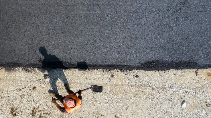 VISUELL Design: Straßen.NRW stand at InfraTech 2026: A documentary-style image shows an employee carrying out asphalt work from a bird’s-eye view; it employs a clear visual language and strong contrasts.