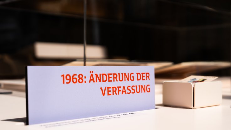 VISUELL Szenografie: Wanderausstellung „Jubiläum. 75 Jahre Verfassung NRW“ für die Stiftung Haus der Geschichte Nordrhein-Westfalen VISUELL Szenografie: Wanderausstellung: Nahaufnahme eines Ausstellungsschildes mit der Aufschrift „1968: Änderung der Verfassung“, daneben kleine Box mit thematischen Karten.
