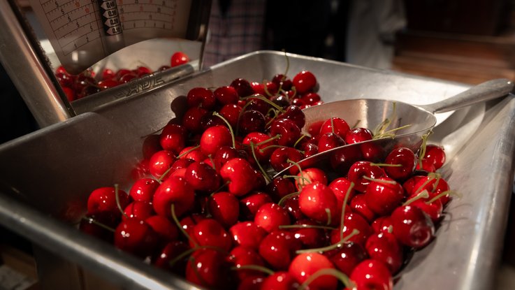 VISUELL Scenography: Permanent exhibition at Hornmoldhaus: Detail of a historical shop scale with fresh cherries in a metal bowl. The exhibit illustrates the trading, weighing and sale of food in a merchant's shop.