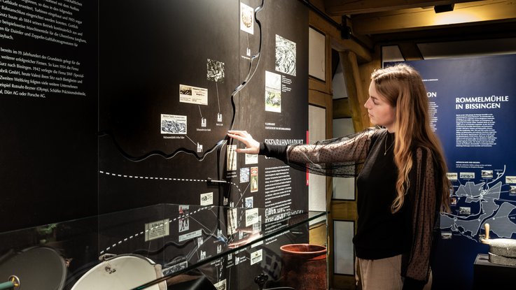 VISUELL Scenography: Permanent exhibition at Hornmoldhaus: Visitors interact with a large-format black timeline featuring historical images and texts. Additional exhibits are integrated into the chronological presentation under a glass cover.