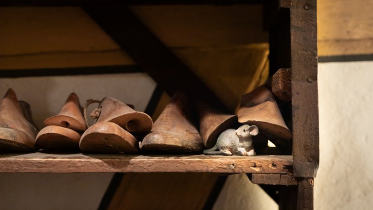 VISUELL Scenography: Permanent exhibition at Hornmoldhaus: Detail of a historical workshop display with wooden shoe lasts on a shelf. A small mouse figure sits between the exhibits as a playful exhibition element.