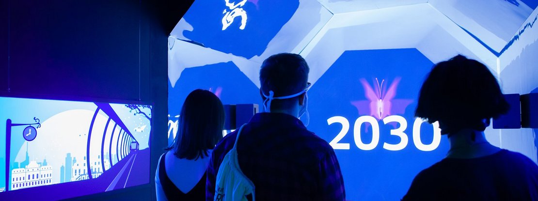 VISUELL Szenografie: Escape-Ausstellung: Besucher stehen im blauen Zeitzug auf dem Weg ins Jahr 2030