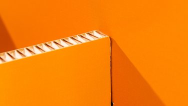 VISUELL Szenografie: Wanderausstellung „Common Grounds – Über Grenzen mitgestalten“ für die Robert Bosch Stiftung GmbH VISUELL Szenografie: Wanderausstellung Robert Bosch Stiftung GmbH: Detail eines modularen Ausstellungselements mit orangefarbener Rückwand und sichtbarer Kante der Wabenplatte;