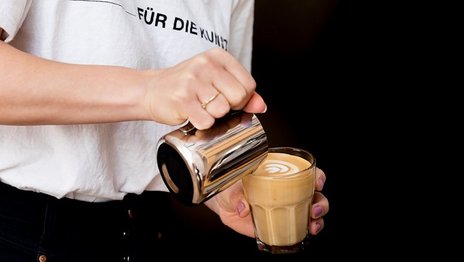 VISUELL Blogbeitrag: Kaffeegenuss: In ein Glas voll Kaffee wird Milch als Latte-Art gegossen