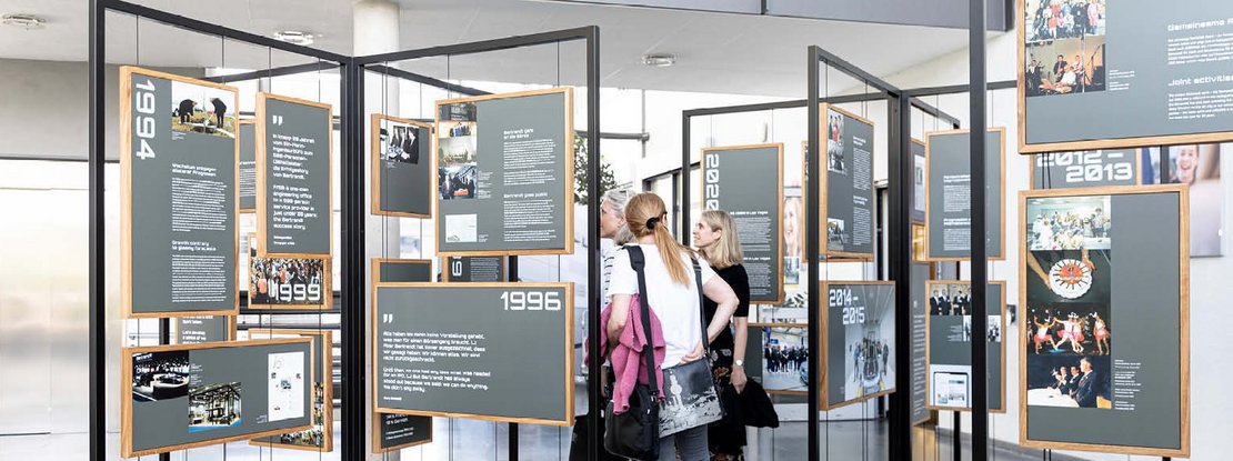 VISUELL Szenografie: Jubiläumsausstellung: Drei Besucherinnen stehen inmitten der Ausstellung und betrachten die Inhalte.