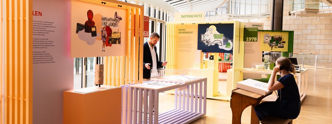 VISUELL Szenografie: Wanderausstellung: Besucher:innen interagieren mit farbig gestalteten Modulen zu Themen Bildung, Datenschutz und Umwelt. Lichtdurchfluteter Raum mit klarer, modularer Gestaltung und grafischen Wandelementen.